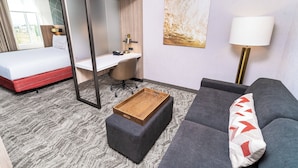 Una habitación de hotel con cama, escritorio, sofá y una pequeña mesa de madera.