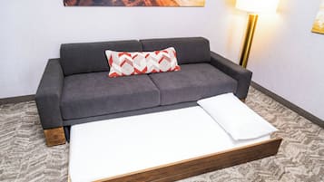 Ein graues Sofa mit Holzrahmen, einem gemusterten Kissen und einer weißen Bettdecke.