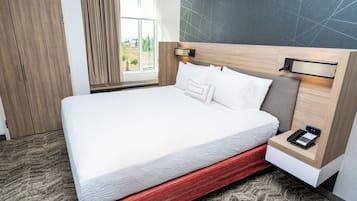 Habitació d'hotel moderna amb un llit gran, un panell de fusta al capçal, una taula de nit amb un telèfon i vista a l'exterior per una finestra.