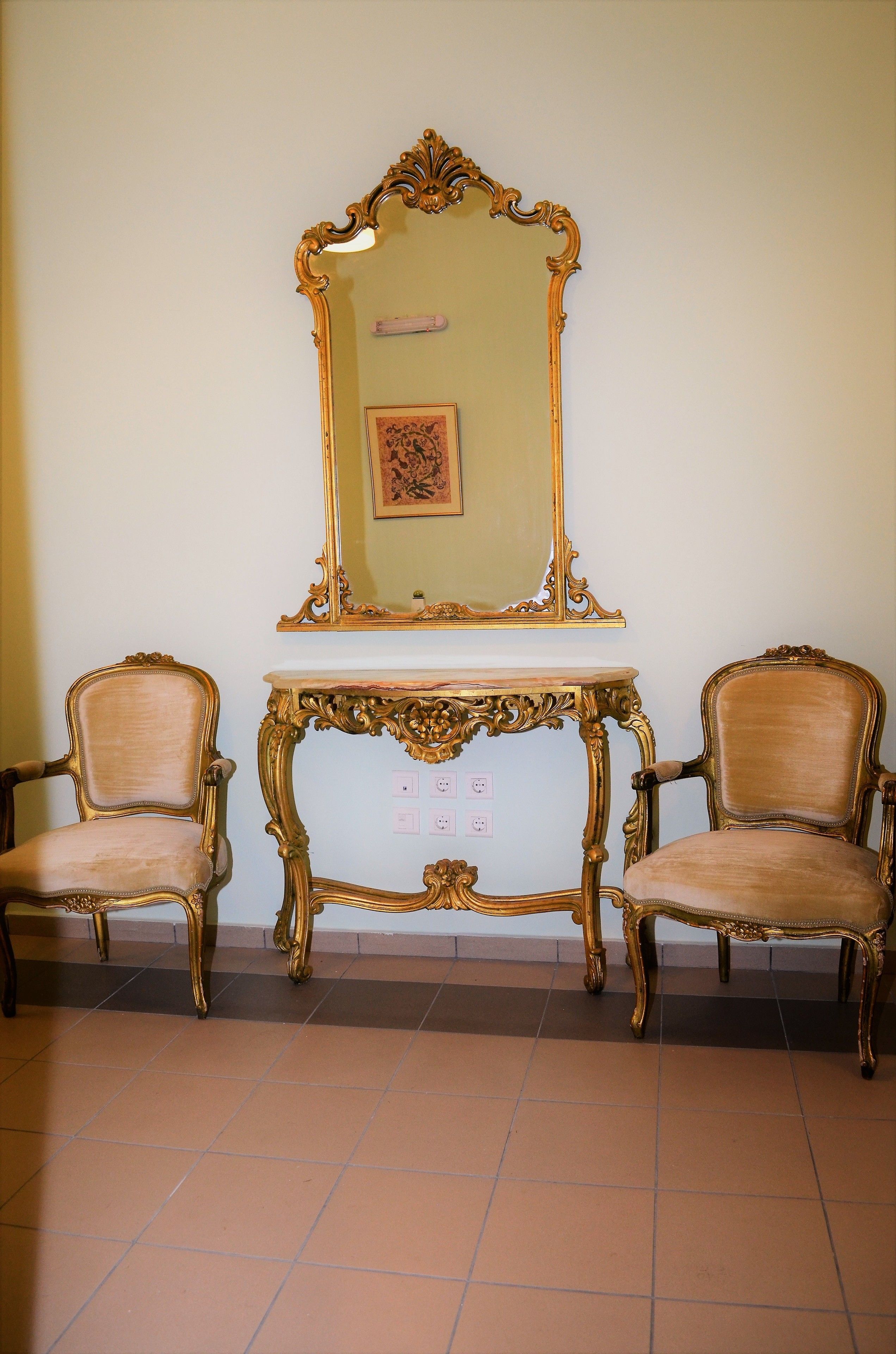 Une pièce comprenant deux fauteuils richement décorés, un miroir encadré d’or et une petite table.