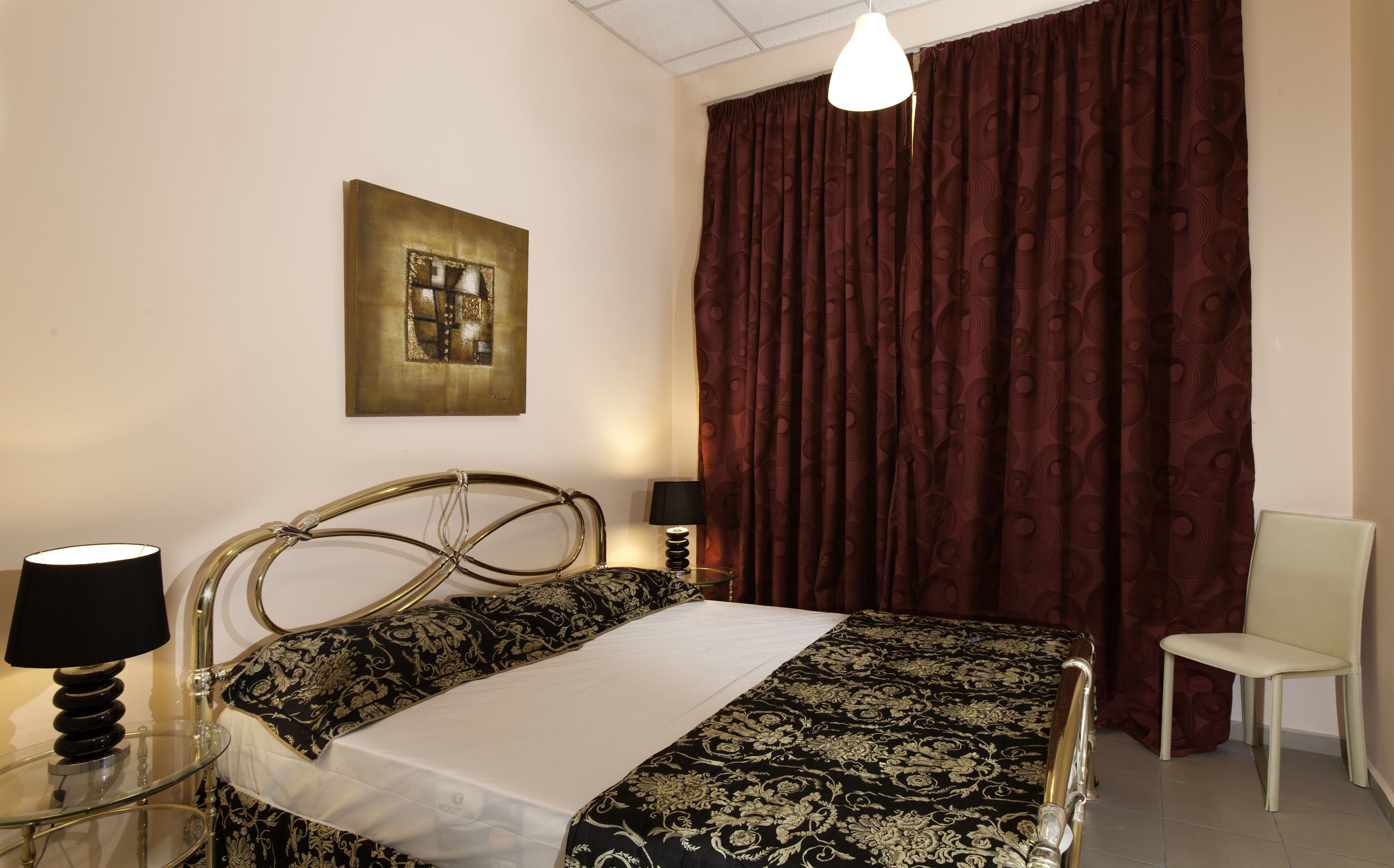A hotel room with a bed, a chair, a lamp, a painting, and a window with curtains.