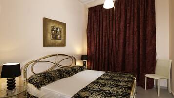 A hotel room with a bed, a chair, a lamp, a painting, and a window with curtains.
