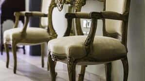 A row of ornate, antique-style chairs with high backs and cushioned seats, arranged in a hallway with tiled flooring and a mirror on the wall. - City center house in Rhodes (Rhodes)