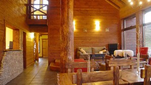 A spacious wooden interior with a high ceiling, a stone wall, and a cozy seating area with a fireplace. - Kaulem Hotel Boutique (El Chalten)