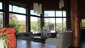 A spacious room with large windows, wooden flooring, and a mix of seating areas including a sofa and chairs. - Kaulem Hotel Boutique (El Chalten)