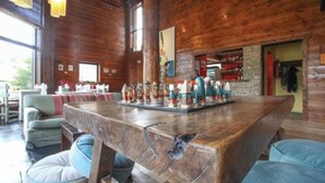 A rustic wooden interior with a long bar, cushioned seating, and large windows. - Kaulem Hotel Boutique (El Chalten)