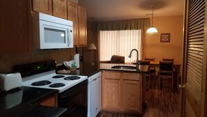 A compact kitchen with a microwave, stove, and dishwasher. There is a dining area with a table and chairs. - Creekside Village (Basye)
