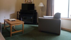 A hotel room with a television on a stand, a lamp, a sofa, and a small table. - Creekside Village (Basye)