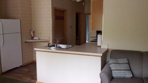 A compact kitchen with a refrigerator, a sink, and a small countertop. There is a sofa with a striped pillow in the living area. - Creekside Village (Basye)