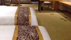 Hotellihuone, jossa on kaksi sänkyä, työpöytä, tuoli ja sohva.