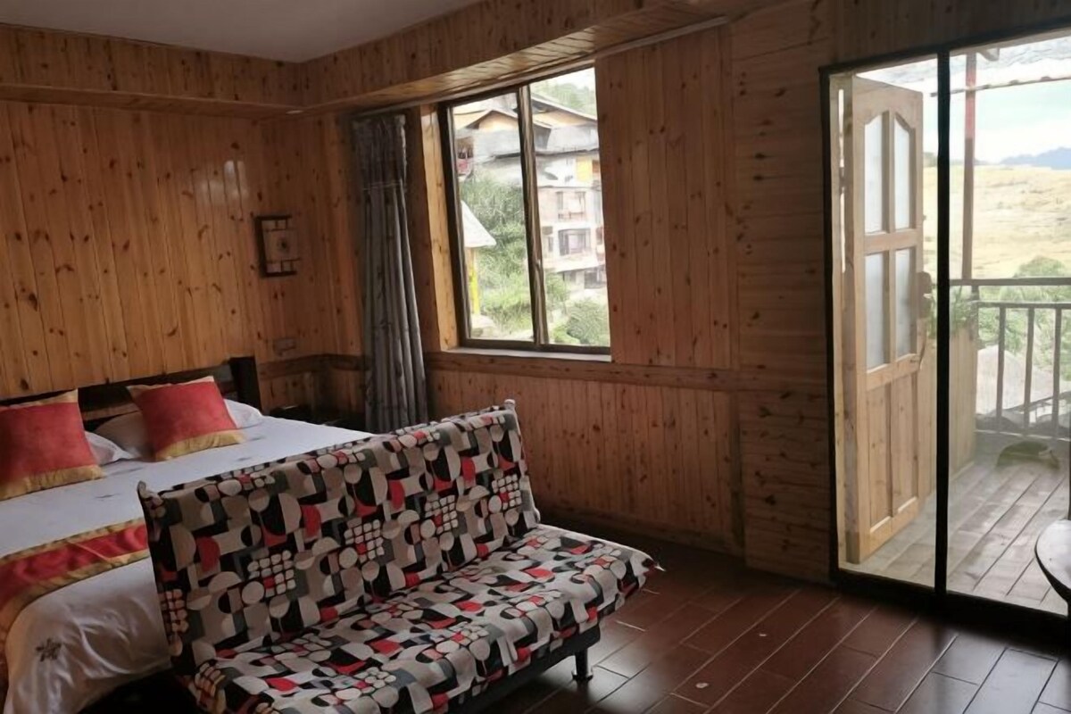 A wooden-paneled room with a bed, a patterned sofa, a large window, and a sliding door to an outdoor area.