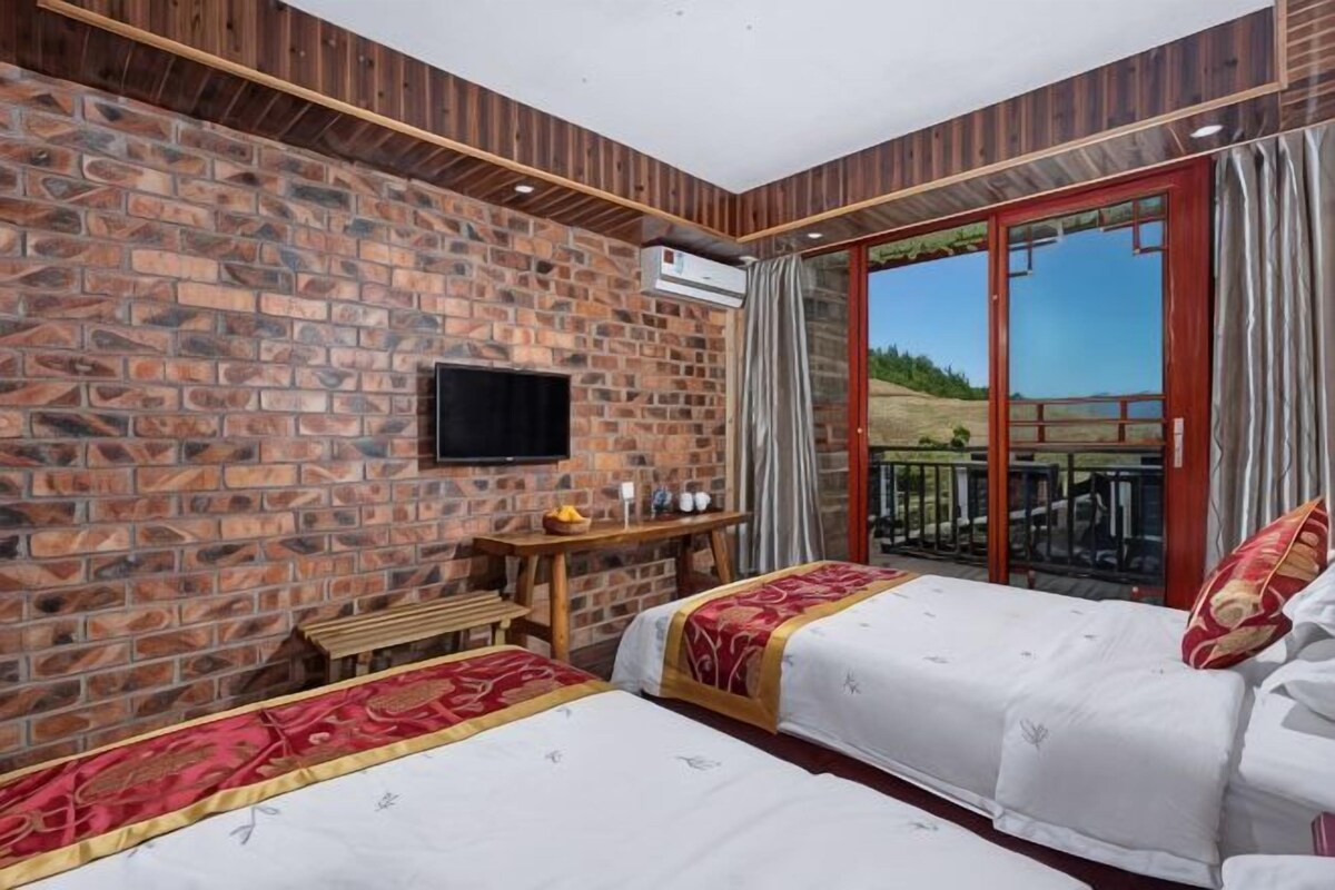 A room with two beds, a TV, a wooden desk, and a balcony with a view.