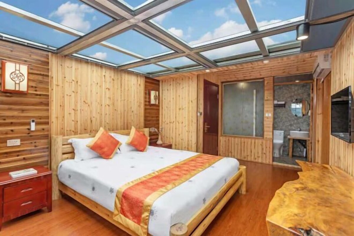 A wooden room with a bed, a wooden table, and a glass ceiling.