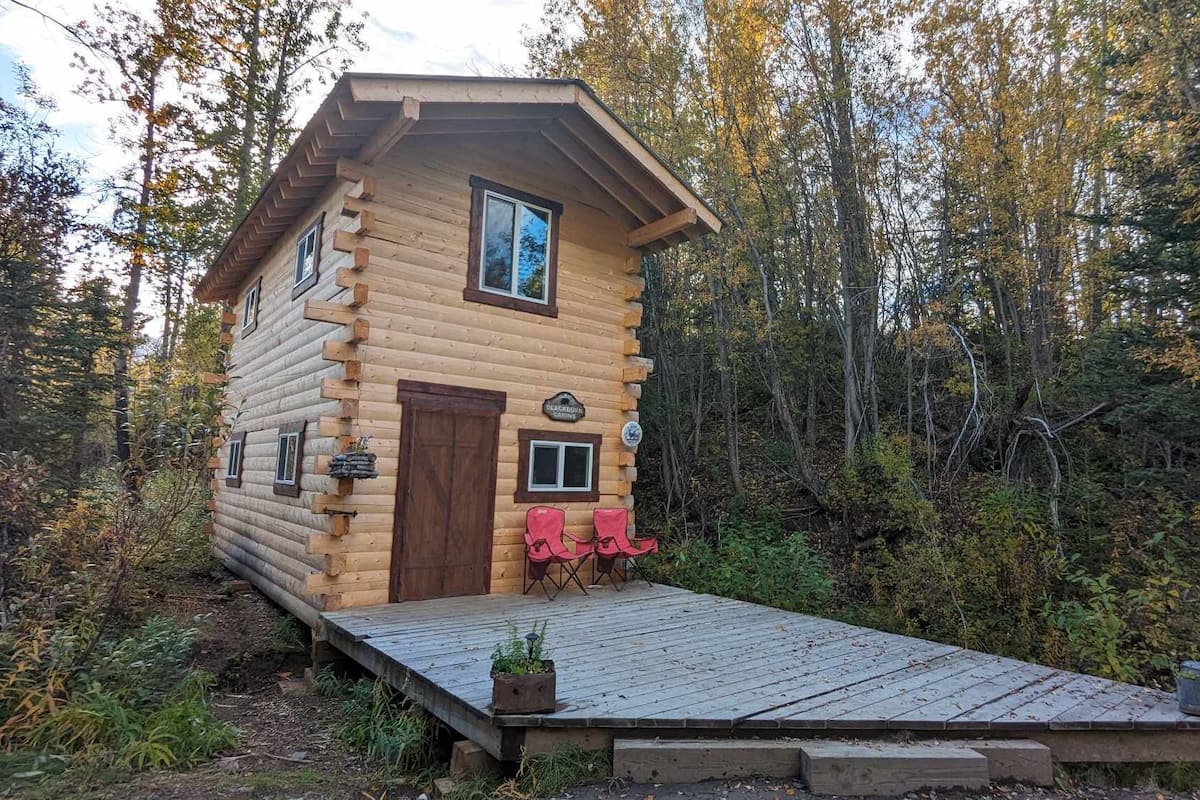 Une cabane en rondins avec une terrasse en bois, une porte et une petite fenêtre.