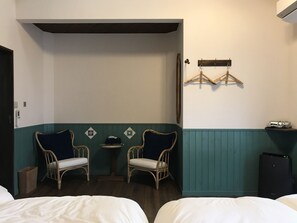 A hotel room with two wicker chairs, a small table, a bed, and a minibar. - CōBō Hostel (Kyoto)