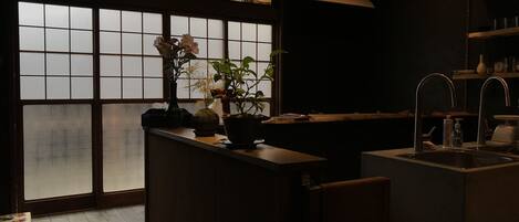A dimly lit kitchen with a large window, a sink, and a countertop with a vase of flowers.