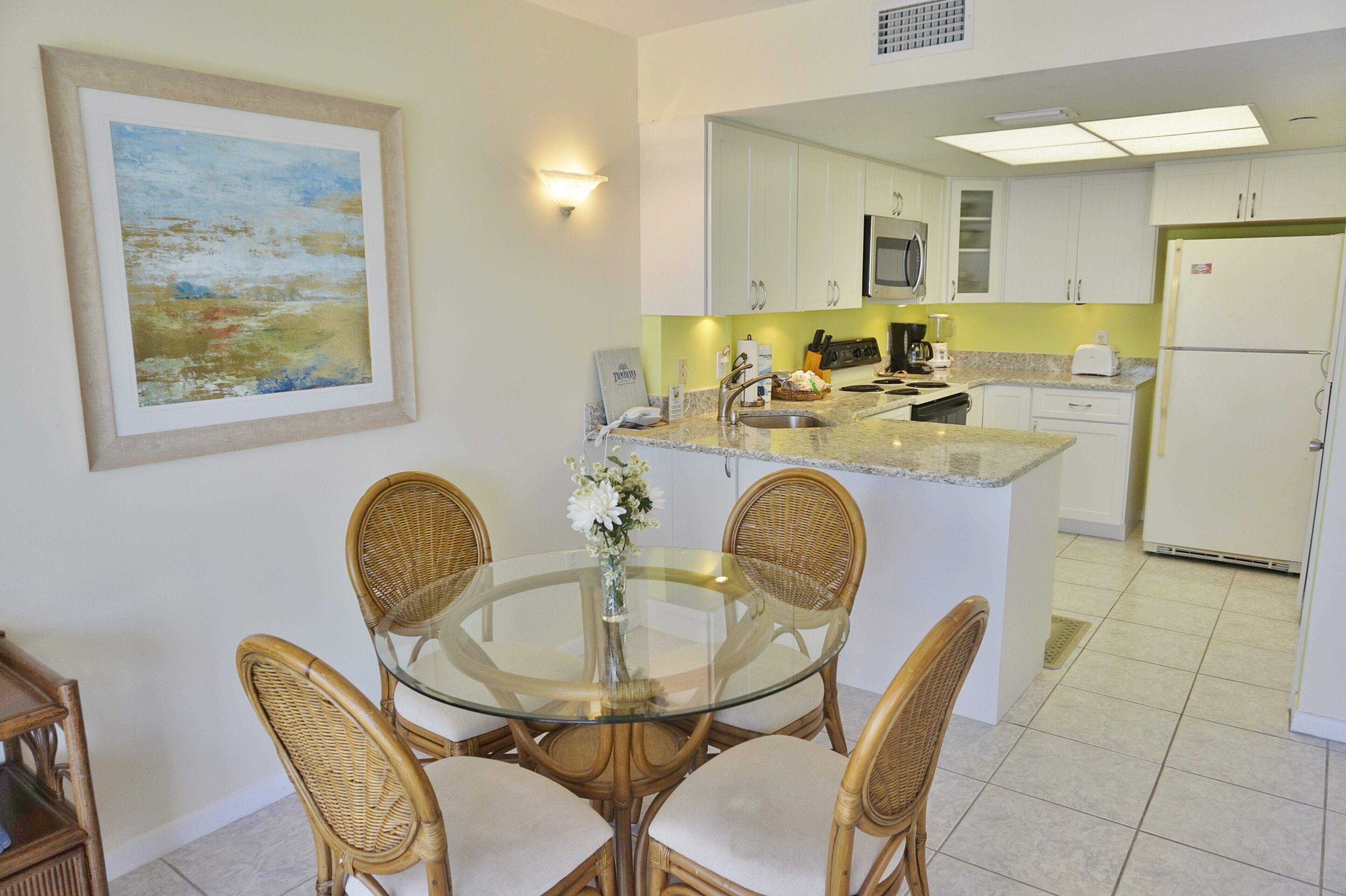 A modern kitchen with white cabinets, a granite countertop, and a dining area with wicker chairs and a glass table.