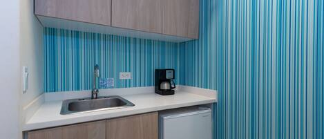 A kitchen with a white countertop, a stainless steel sink, a coffee maker, and a white refrigerator.