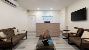 Zona de recepción de hotel con mostrador, dos sofás, una mesa de centro y un televisor de pantalla plana.