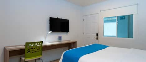 Een hotelkamer met een bed, een bureau met stoel, een televisie en een raam met uitzicht.
