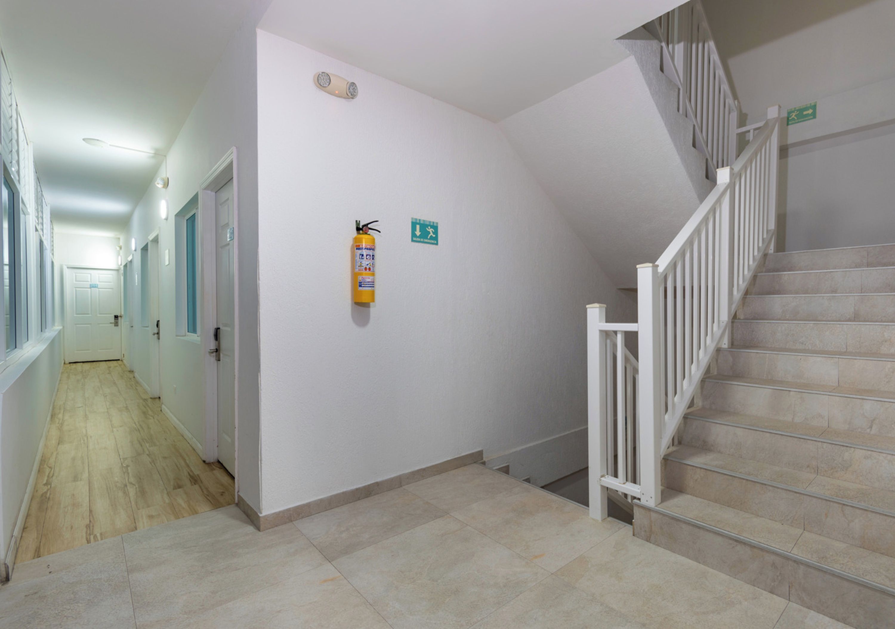 Un couloir avec un extincteur fixé au mur, un escalier muni d’une rampe et une porte au bout.