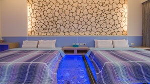 Habitación de hotel con una cama que presenta un diseño de acuario iluminado en azul, una pared con un motivo circular y una mesita de noche con lámpara.