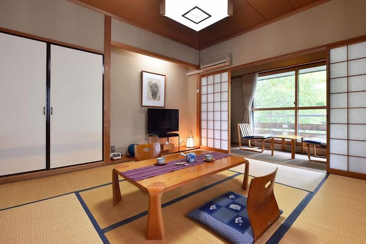 Una habitación japonesa tradicional con suelo de tatami, una mesa baja, un televisor y puertas correderas.