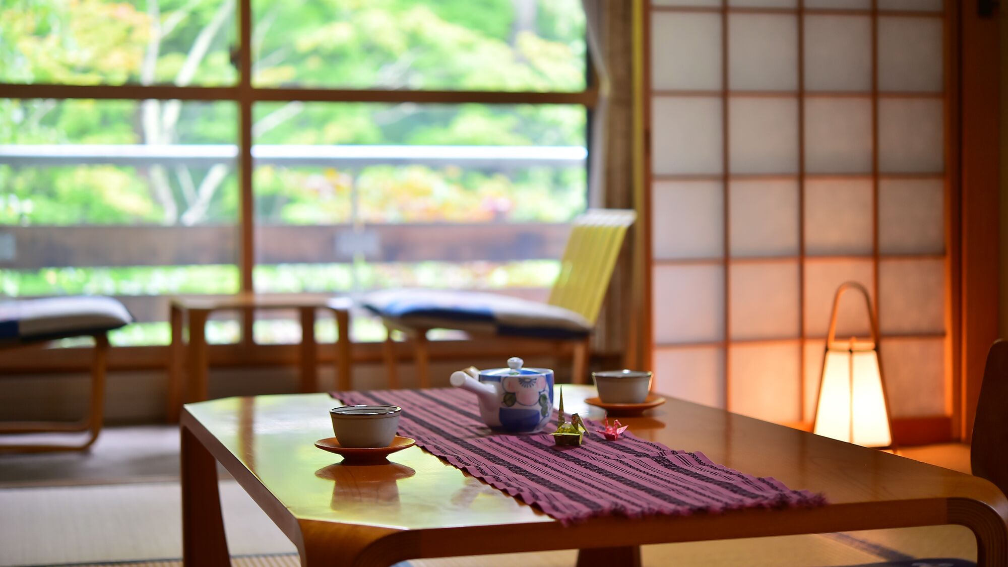 A traditional Japanese room with tatami flooring, a low table with a tea set, a chair, and a view through a shoji screen.