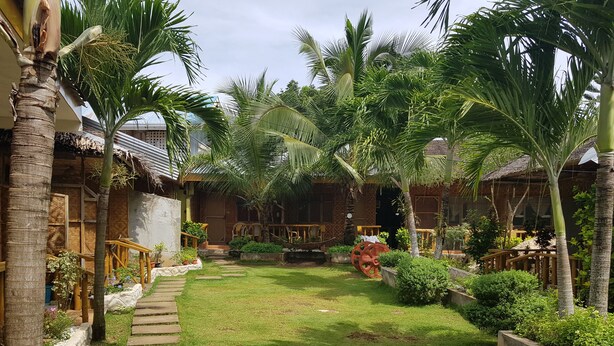 A tropical garden with palm trees, a stone pathway, and a thatched-roof building. - Alona Bamboo House (Panglao)