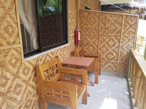 A wooden outdoor seating area with a table and chairs, a window with a view, and a fire extinguisher mounted on the wall. - Alona Bamboo House (Panglao)