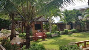 A well-maintained garden with a palm tree, a wooden bench, and a small hut. - Alona Bamboo House (Panglao)