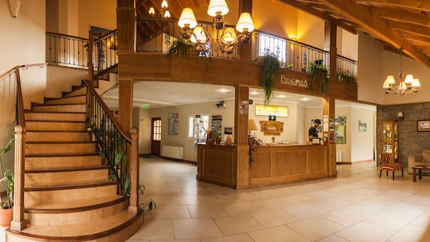 A spacious lobby with a wooden staircase, a reception desk, and a balcony with hanging plants.