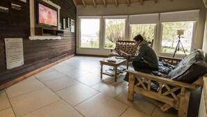 A cozy room with a wooden ceiling, a television mounted on the wall, a sofa, and a small table with magazines.