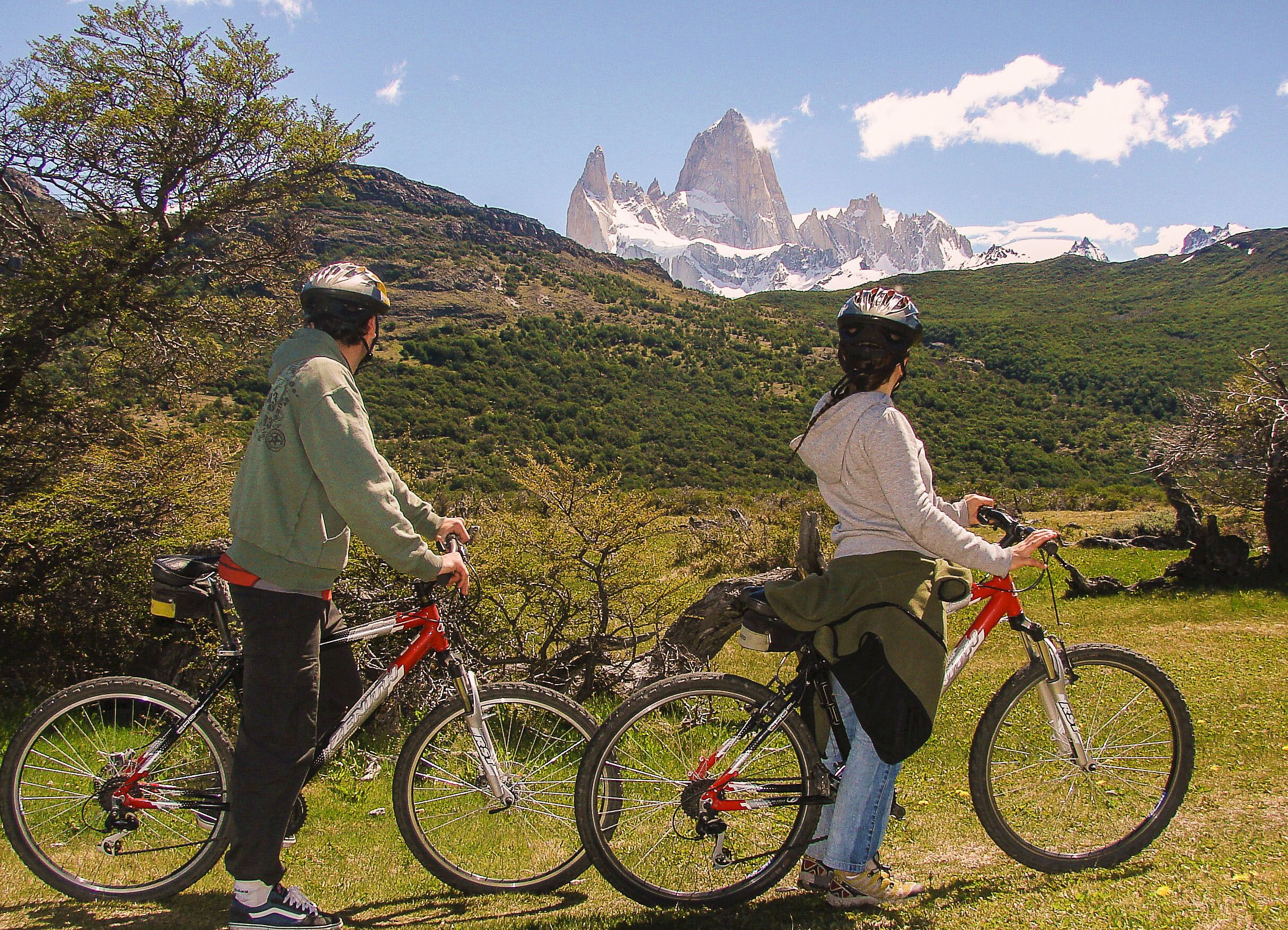 Two people on bicycles with a mountainous landscape in the background.