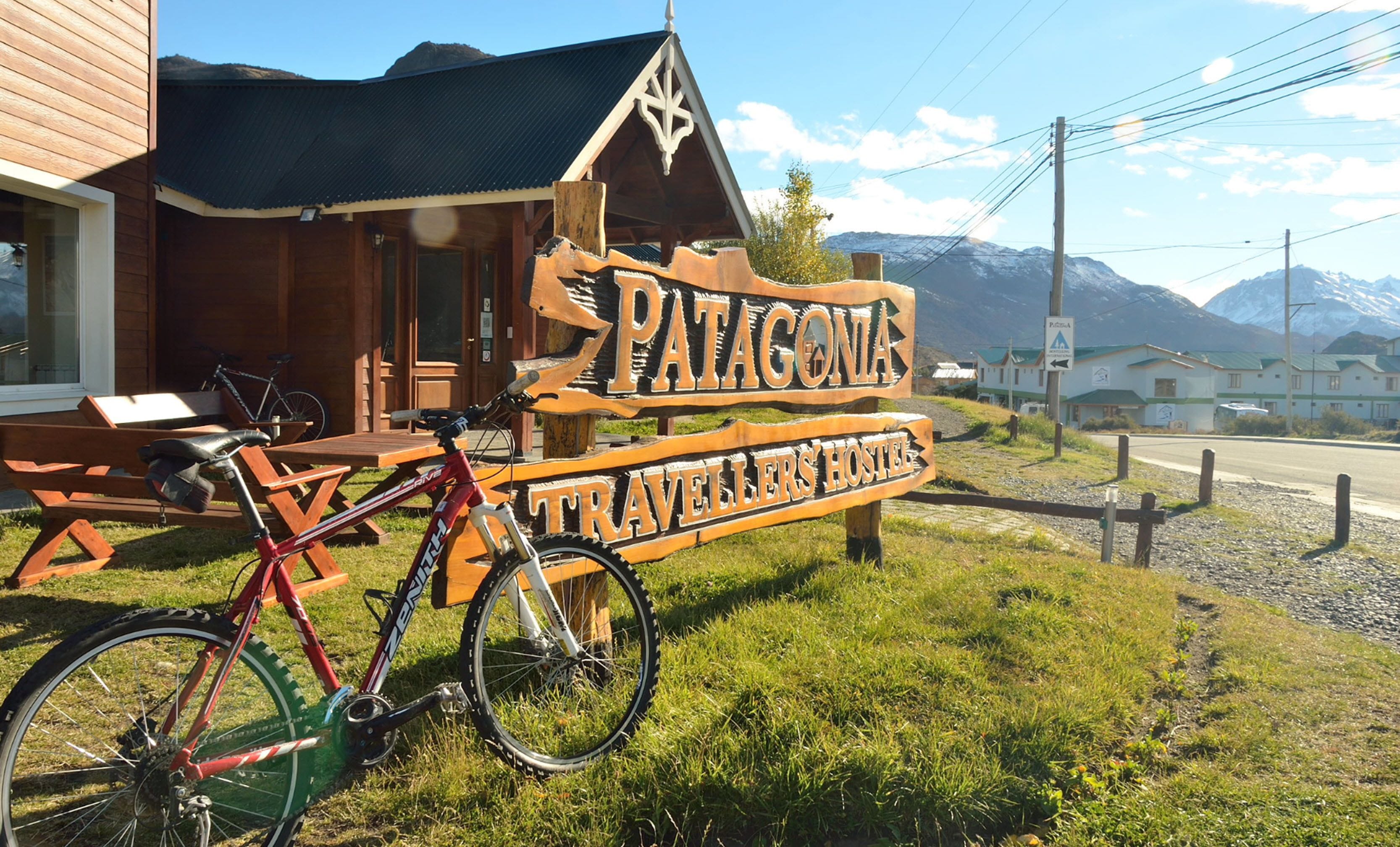 Un letrero de madera que dice 'Patagonia Travellers' Hostel' con montañas al fondo.
