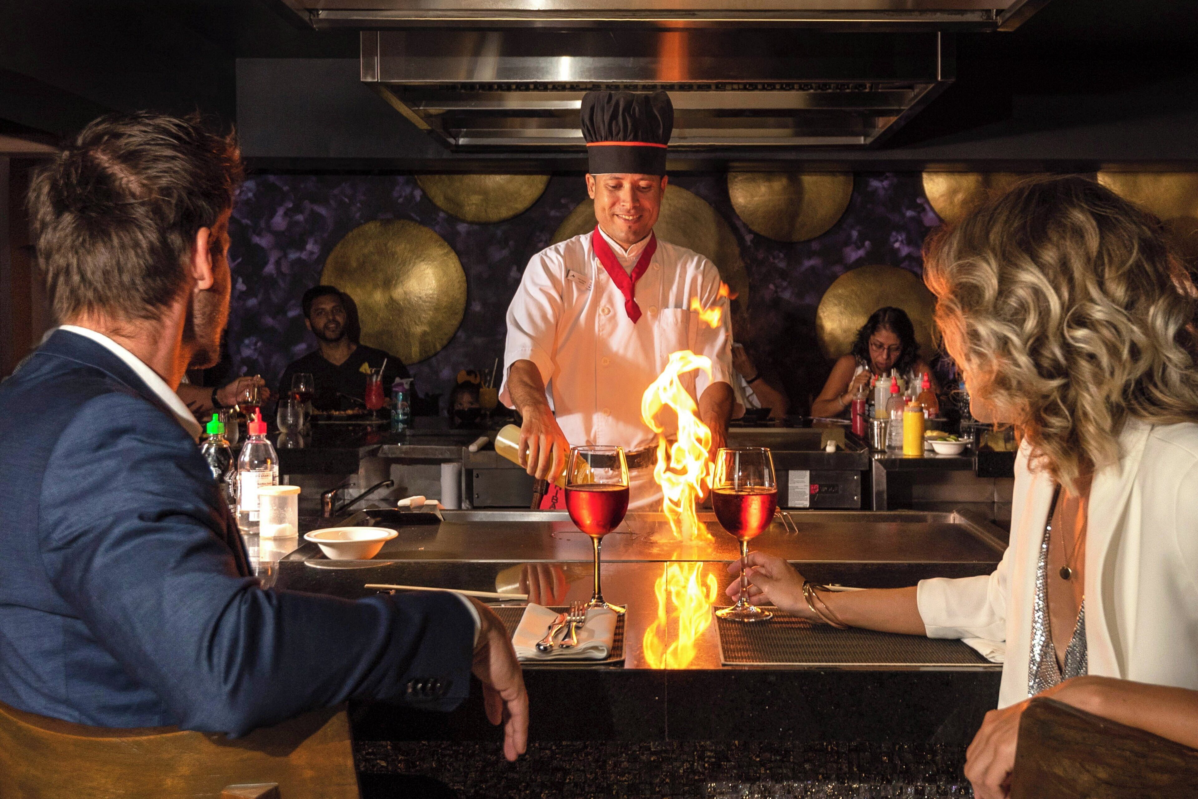 Un chef prépare un plat flambé au bar, sous le regard des clients.