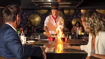 Un chef prépare un plat flambé au bar, sous le regard des clients.