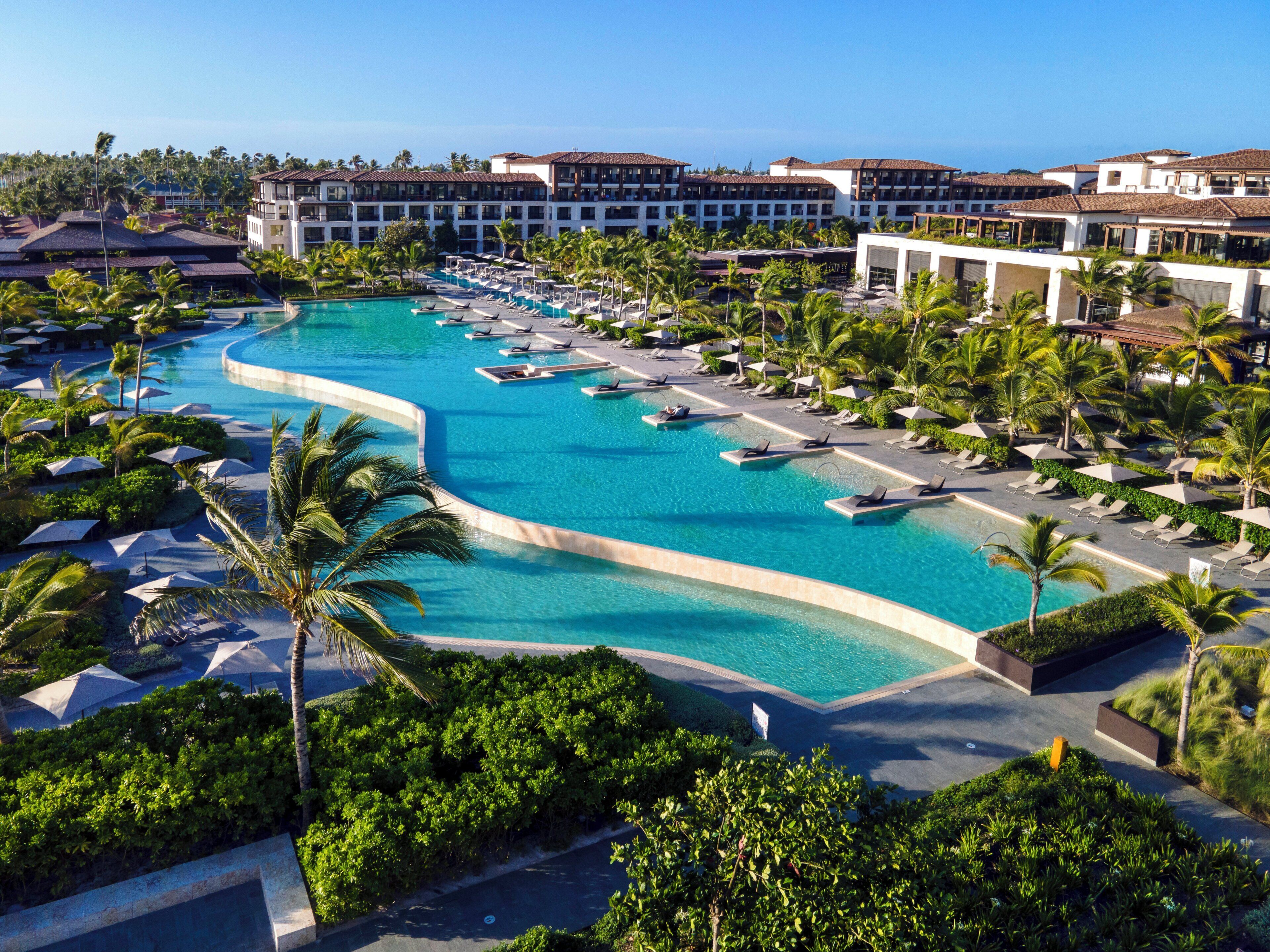A resort with a large pool, lounge chairs, and palm trees.