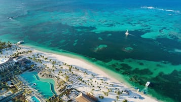 Vue aérienne d’un complexe hôtelier avec une plage, des eaux turquoise et cristallines, et une piscine.