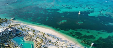 An aerial view of a resort with a beach, clear turquoise waters, and a swimming pool.