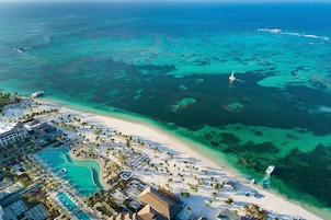 An aerial view of a resort with a beach, clear turquoise waters, and a swimming pool.