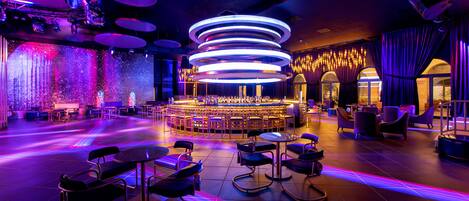 A modern bar area with circular seating and a central stage, surrounded by tables and chairs.