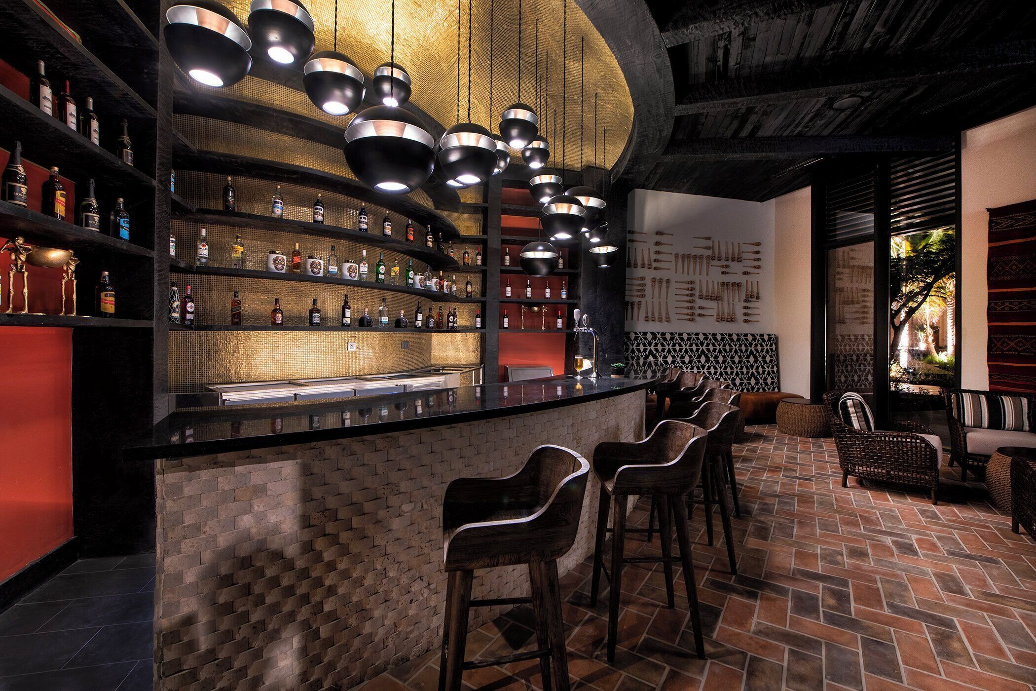 A bar area with a brick wall, shelves of bottles, hanging pendant lights, and bar stools.
