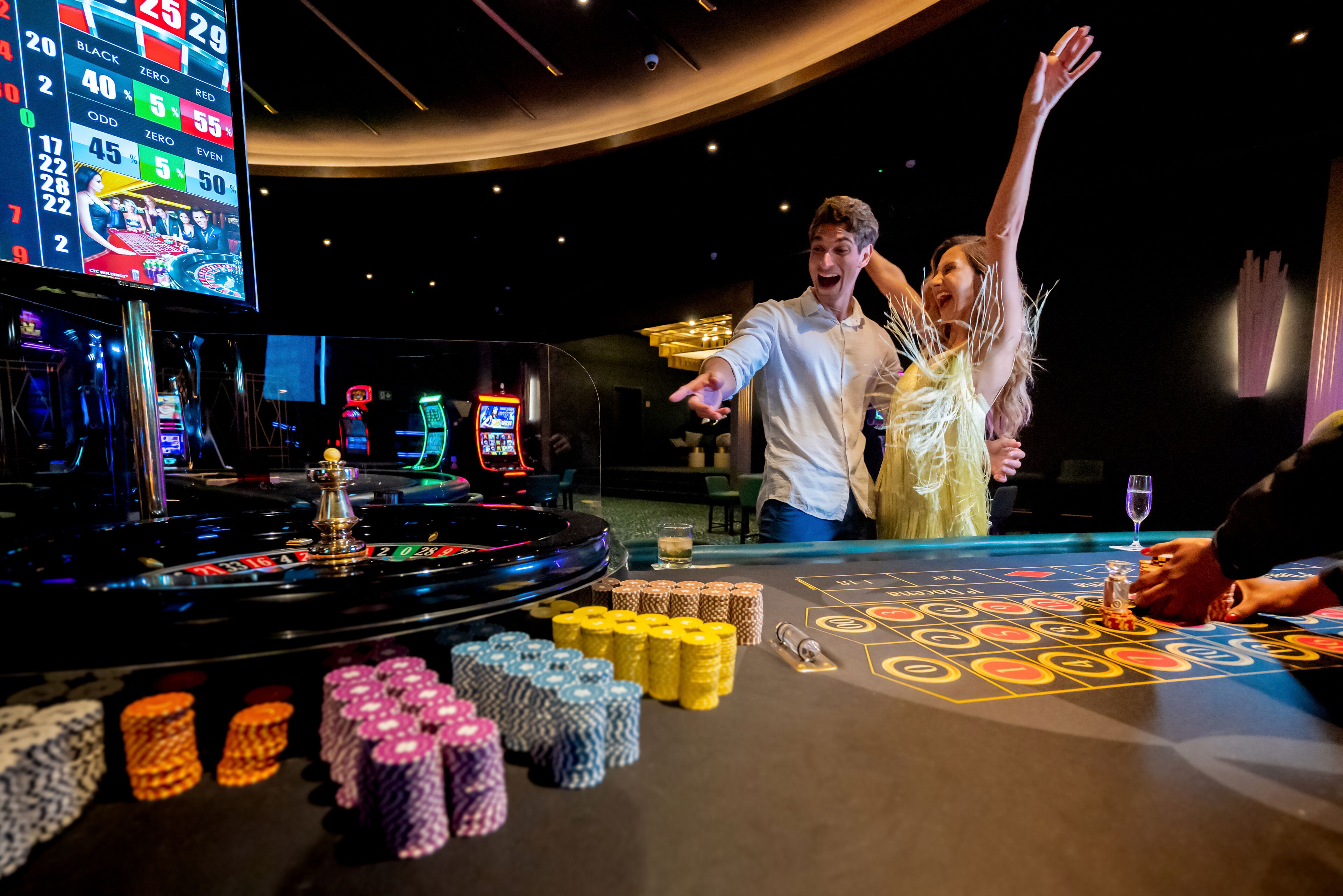 Une salle de casino avec une table de roulette, des jetons et un grand écran affichant les probabilités de gain.