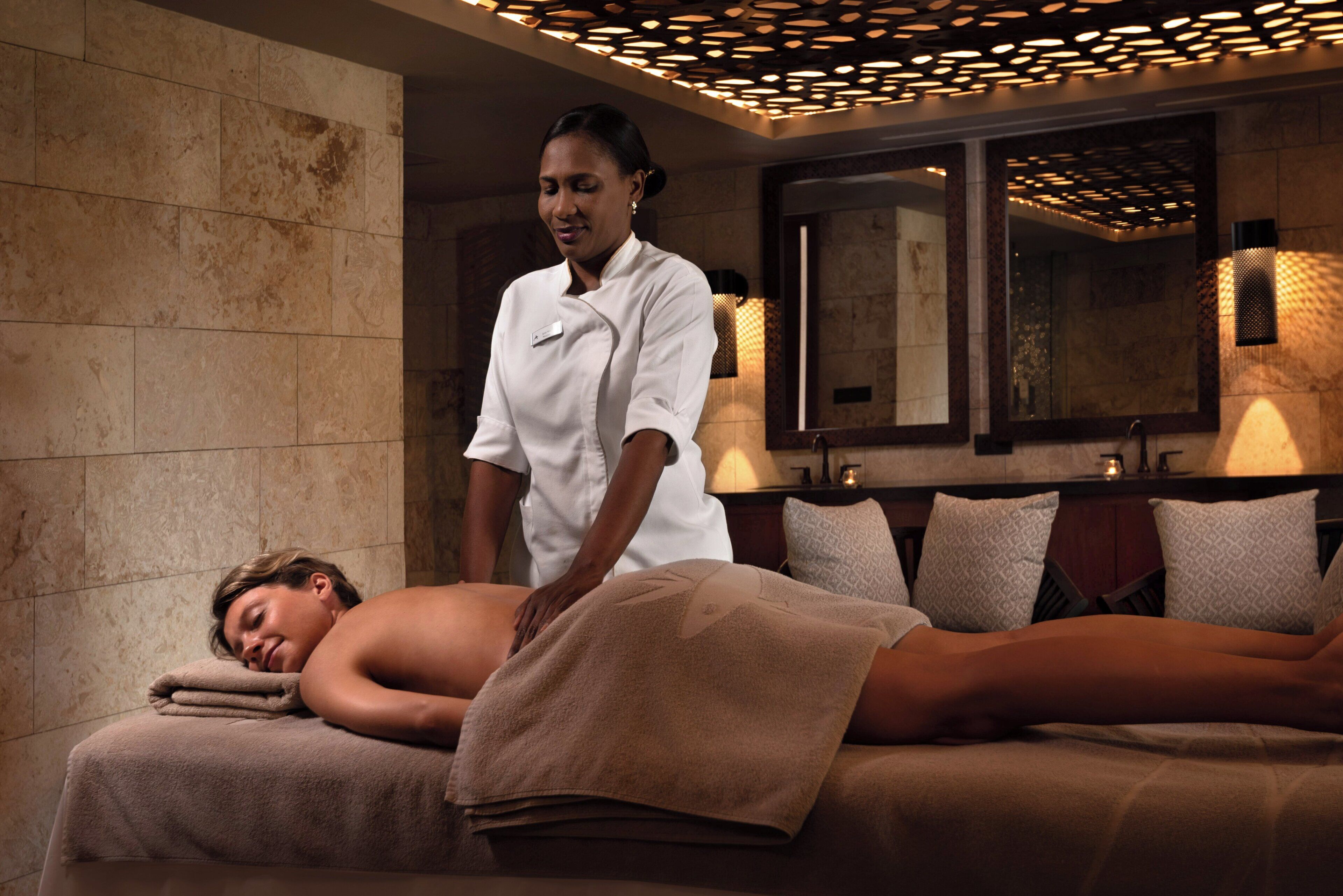 Een massageruimte met een massagetafel, handdoeken en een massagetherapeut.