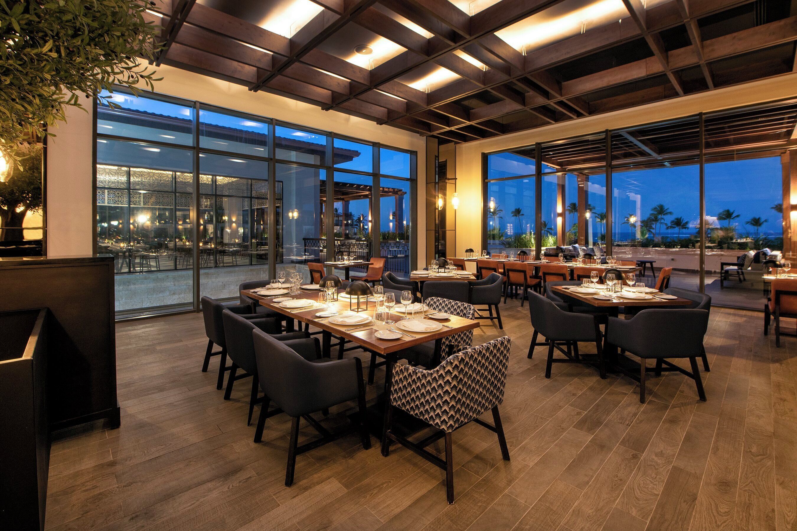 Un restaurante con varias mesas, sillas y vistas panorámicas de la ciudad a través de amplios ventanales.