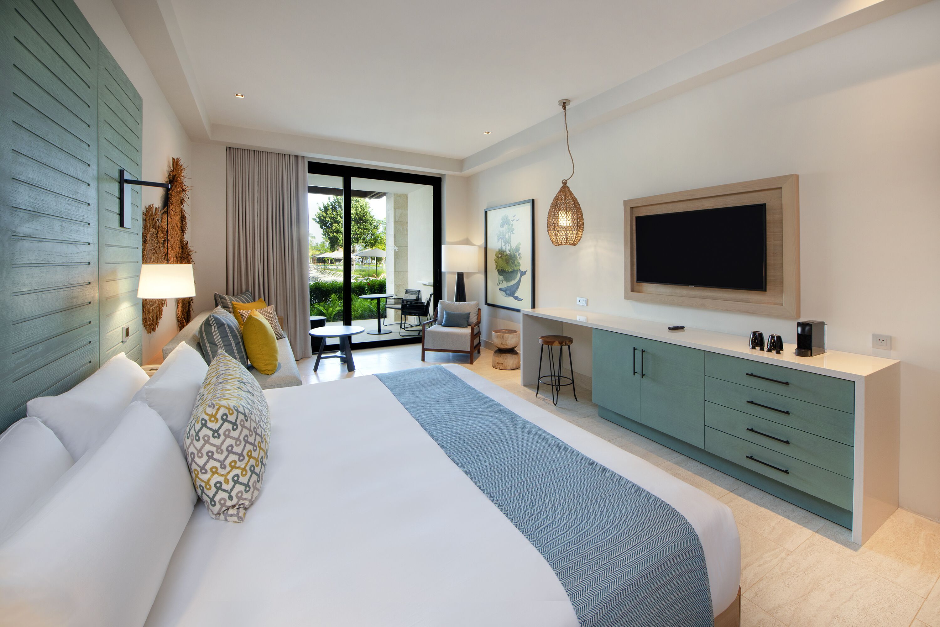 Une chambre d’hôtel moderne dotée d’un grand lit, d’une télévision, d’une kitchenette et d’un balcon avec coin salon extérieur.