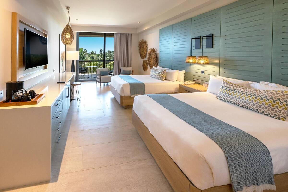 A hotel room with two beds, a TV, a desk with coffee-making equipment, and a balcony with a view.