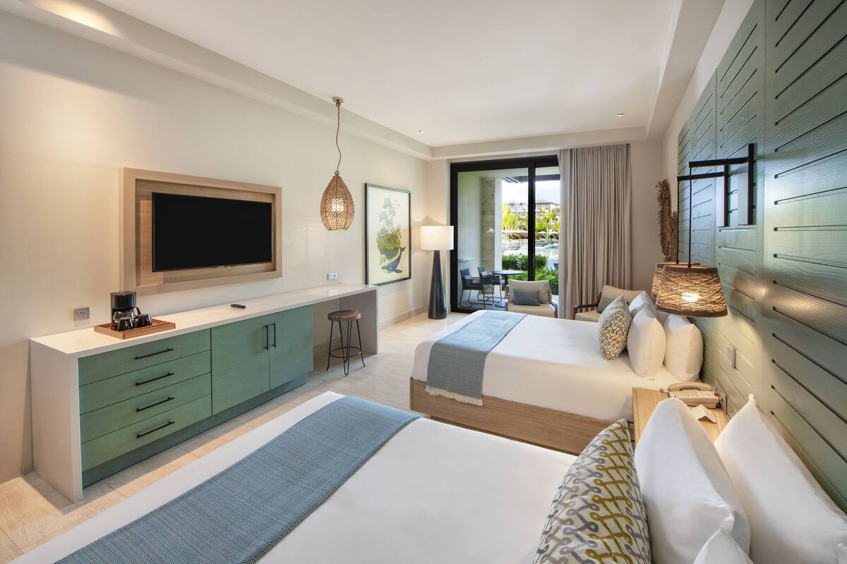 A hotel room with two beds, a TV, a desk, and a view of the outdoors.