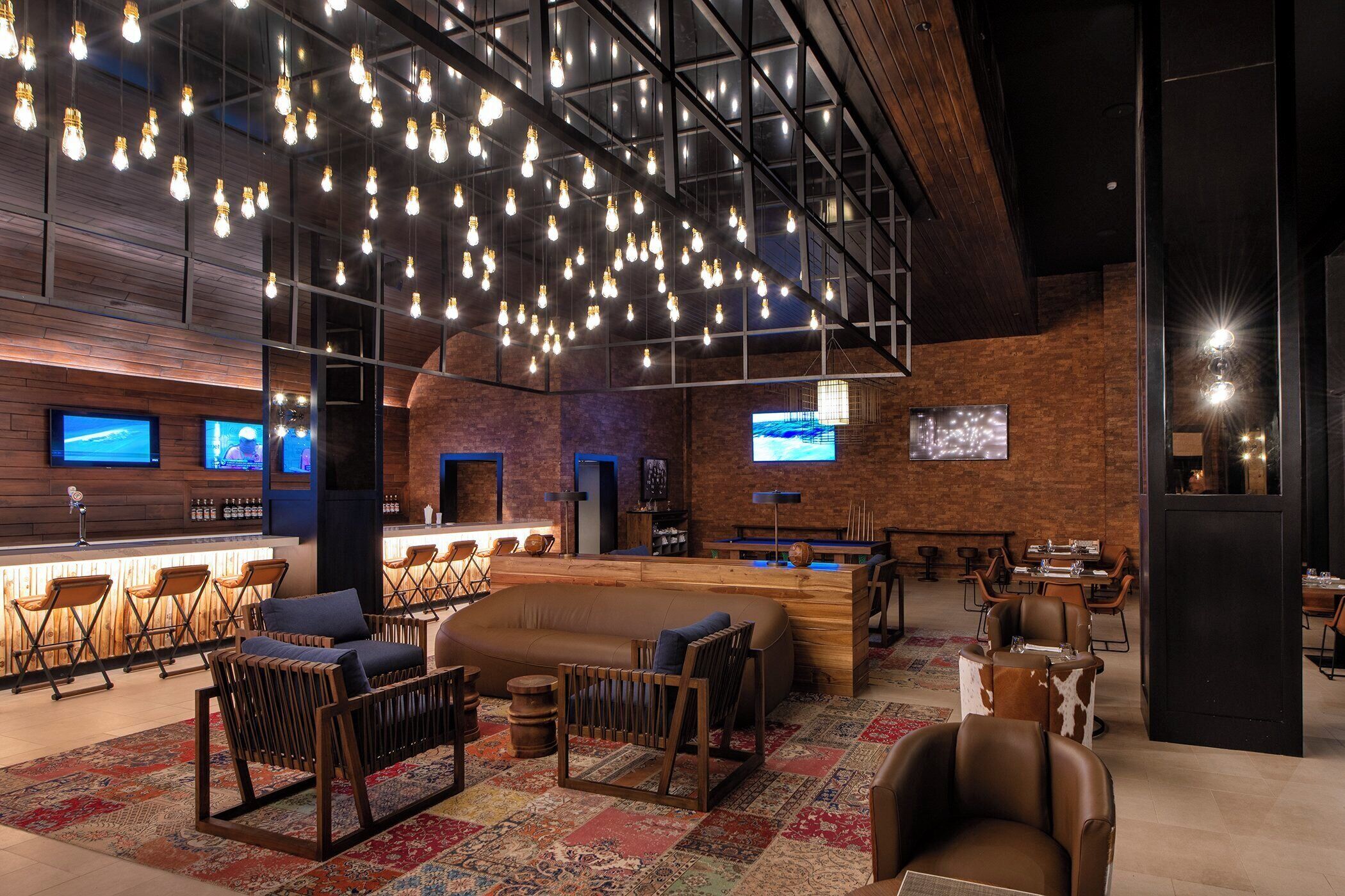 A modern bar area with hanging light fixtures, seating, and a television screen.